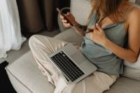 Kaboompics - Woman Using a Phone with a Laptop on Her Lap at Home
