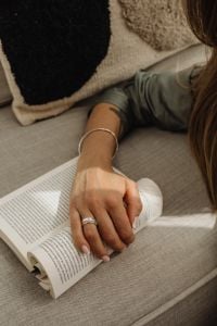 Kaboompics - Ringed Hand Resting on an Open Book and Light Knit Pants on Sofa