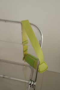 Kaboompics - Lime Green Crossbody Bag Draped Over Clear Chair Against Neutral Wall