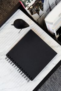 Kaboompics - Black Spiral Notebook and Wooden Bird Sculpture beside Design Books on Marble