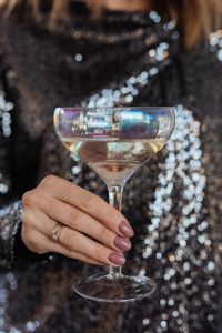 Kaboompics - Iridescent Champagne Coupe and Ringed Hand Against a Dark Sequin Party Backdrop