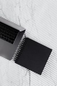 Kaboompics - Black Notebook beside Laptop on White Marble, Portrait Workspace Flat Lay