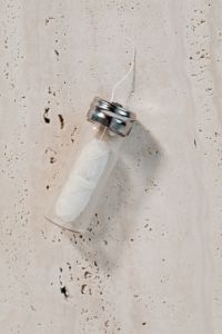 Kaboompics - Glass Dental Floss Dispenser on Textured Beige Stone, Minimal Zero-Waste Bathroom Product Photo