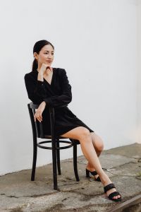 Kaboompics - Asian Woman Sitting with Hand under Chin in Black Dress and White Wall