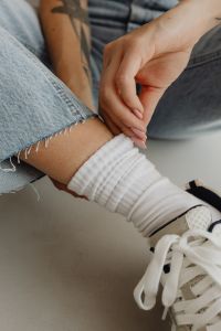 Kaboompics - Hands Adjusting White Ribbed Sock beneath Frayed Jeans Hem, Close-Up Casual Styling