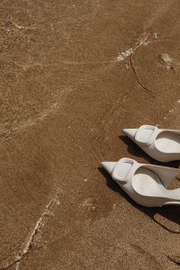 Kaboompics - White Buckle Mules on Sand with Copy Space