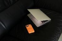 Kaboompics - Orange Smartphone and Half Open Laptop on Black Leather Sofa