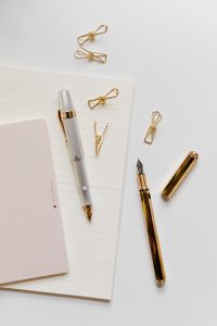 Kaboompics - Overhead Stationery Flat Lay with Silver and Black Fountain Pens, Gold Clips, Lined Notebook and Pink Notepad