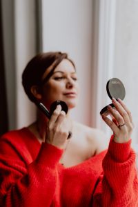 Kaboompics - A woman in a red sweater does her make-up - applies a foundation with a brush