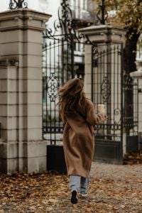 Kaboompics - Woman in Camel Coat Walking Toward an Ornate City Gate
