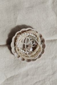 Kaboompics - White Pearl Necklaces in Scalloped Ceramic Bowl on Beige Linen, Minimal Background with Copy Space