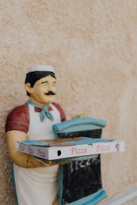 Kaboompics - Pizzeria Figurine Holding a Pizza Box, Italian Street Detail