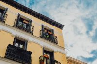 Kaboompics - Yellow Apartment Facade with Iron Balconies and Potted Plants Against Blue Sky