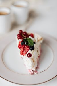 Kaboompics - Berry Pavlova Slice on a White Plate with Coffee Cups in Soft Focus