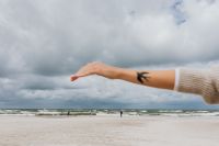 Kaboompics - Swallow Tattooed Arm Over the Beach, Cloudy Seascape Background for Coastal Travel Content
