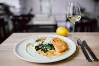 Kaboompics - Bourbon Glazed Salmon Dinner with White Wine Glass and Lemon in Soft-Focus Restaurant