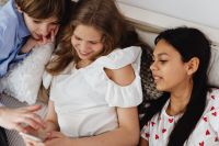 Kaboompics - Three Teen Friends Gathering Around a Smartphone on a White Bed