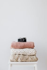 Kaboompics - Folded Sweaters With Vintage Camera on White Stool