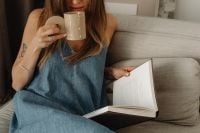 Kaboompics - Woman Reading an Open Book with Coffee on the Sofa