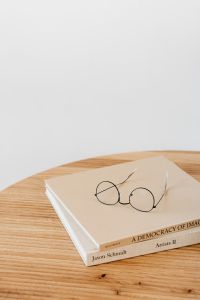 Kaboompics - Eyeglasses and Open Book on a Wooden Desk with Generous Copy Space