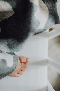 Kaboompics - Newborn Baby's Foot Peeking from Grey Knit Blanket in White Crib