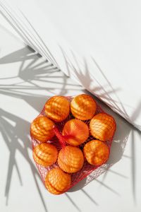 Kaboompics - Diagonal Palm Shadows on White with a Red Mesh Bag of Oranges at Bottom