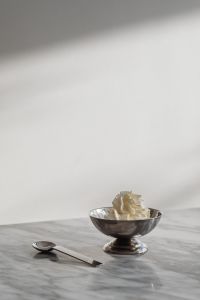Kaboompics - Silver Pedestal Bowl of Whipped Cream and Spoon on Marble with Soft Gray Wall