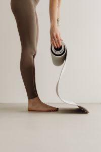 Kaboompics - Standing Woman Holding a Rolled Yoga Mat Against a Wall