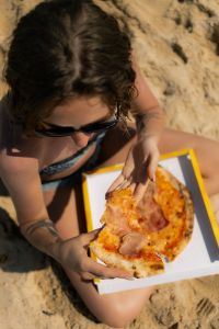 Kaboompics - Close-Up of a Woman Eating Pizza on the Sand