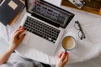 Kaboompics - Overhead View of a Woman Typing on a Laptop and Holding Coffee in a White Bedding Home Office