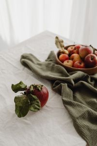 Kaboompics - Wooden Bowl of Mixed Apples on White Linen with Soft Natural Light and a Dried Leaf