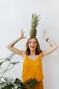 Playful Pineapple Lifestyle Portraits: Smiling Woman in a Mustard Yellow Top on a Bright White Background