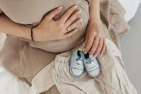 Kaboompics - Close-Up of Pregnant Belly, Hands and Blue Baby Shoes on Beige Dress
