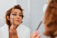 Kaboompics - Middle-Aged Woman Applying Eye Makeup with a Cosmetic Pencil in a Bathroom Mirror