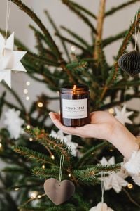 Kaboompics - Hand Holding Amber Glass Candle in Front of a Christmas Tree with Paper Star Ornaments, Cozy Holiday Home Decor