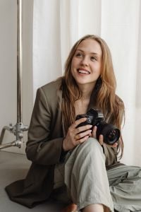 Kaboompics - Smiling Young Female Photographer with DSLR Camera in Neutral Studio
