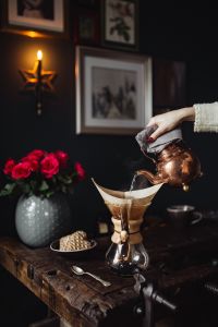 Kaboompics - Woman Pouring Coffee with Chemex beneath a Star-Shaped Wall Light, Red Rose Home Decor