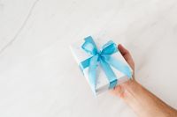 Kaboompics - One Hand Presenting a Snowflake Gift Box with Blue Bow over Marble
