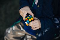 Kaboompics - Hands Solving a Rubik's Cube in a Navy Jacket, Horizontal Close-Up with Outdoor Background
