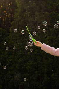 Kaboompics - Hand in Pink Sweater Releasing Soap Bubbles against Dark Garden Background