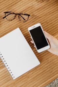 Kaboompics - Hand Using Smartphone with Eyeglasses and Notebook on a Wooden Desk, Lifestyle Workspace