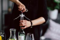 Kaboompics - Hands Using a Corkscrew to Open Wine at a Table with Wine Glasses