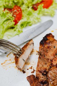 Kaboompics - Fork Lifting Grilled Pork Neck beside Tomato and Lettuce Salad, White Plate Close-Up