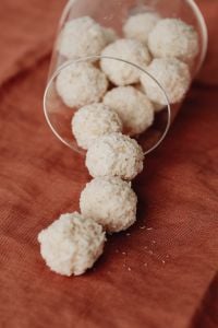 Kaboompics - Vertical Close-Up of Coconut-Covered Truffles in a Glass on Rust Linen, Homemade Candy Still Life