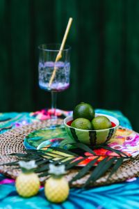 Kaboompics - Bowl of Fresh Limes beside a Water Glass with Straw on Colorful Tropical Table Linens