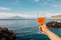 Kaboompics - Handheld Aperol Spritz with Rocky Shoreline in View