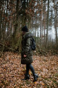 Kaboompics - A woman dressed in a green jacket, a black hat and black trousers with a black backpack in the forest