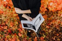 Kaboompics - Close-Up of a Woman Holding an Open Book over Red and Orange Autumn Leaves, Reading Lifestyle Photo