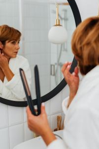 Kaboompics - Middle-Aged Woman Using a Hair Straightener at a Bathroom Mirror, At-Home Hair Care