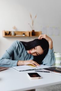 Kaboompics - Tired Asian Woman Writing Notes with Her Head Resting on Her Hand